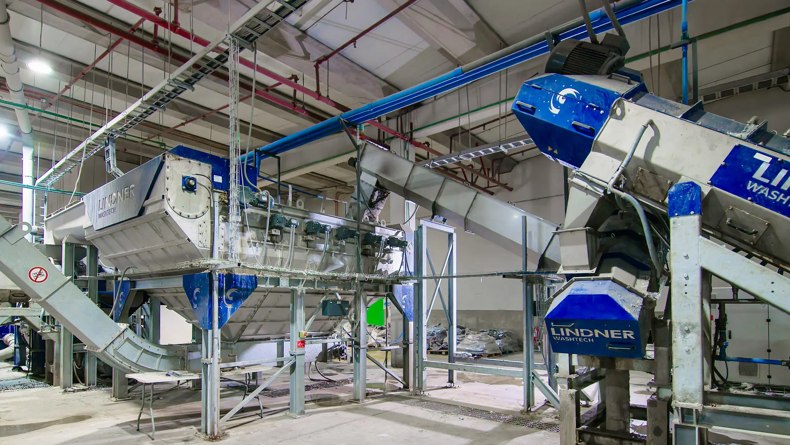 Industrielle Waschmaschine von Lindner Washtech in einer Produktionshalle mit Förderbändern und blauen Rohren.